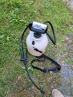 Handheld pump sprayer on grass surface showing full tank, hose, nozzle, and adjustable strap.