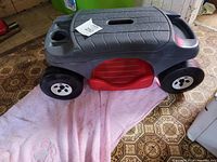Side view of gray Step 2 yard cart with red base and four black wheels on patterned floor.