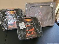 Photo shows two North 49 brand new flyaway wheeled duffle bags in black, each sealed in plastic, and one large gray zippered fabric storage bin.