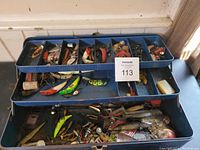 Open blue plastic tackle box showing trays filled with various fishing lures and tackle items.