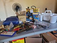Wide view of table with portable paint stripper, assorted hand tools, locks, and other items on grey table surface.