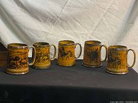 Front view of five ceramic Lord Nelson beer steins lined up showing various embossed historic scenes.