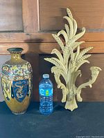 Photo showing both ornate cream-colored decorative candle holders designed with wheat stalk motifs next to a water bottle for scale.