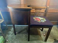 Side view of antique wooden telephone desk alongside wooden chair with floral embroidery on seat.