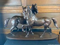 Front side view showing two horses with detailed bronze finish and oval base.