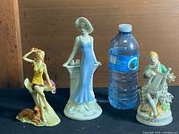 Front view of three vintage porcelain figurines with a water bottle for size reference.