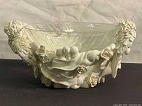 Front view showing full glass bowl atop resin base with one cherub visible holding hands together and detailed feather wings with gold accents.