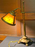 Full side view of the desk lamp with amber shade and brass-finished base sitting on a black surface against a wood paneled background.