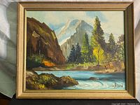 Framed oil painting showing full landscape scene with mountains, trees, river, and rocks.