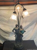 Front view of the vintage table lamp, showing the resin figurines and three art glass shades lit up.