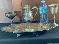 Photo showing the full lot including the silver tray, two chalices, the silver coffee pot with a yellow handle, and a water bottle for scale.