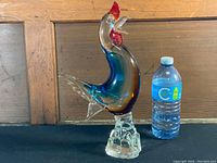 Side view of Murano art glass rooster beside water bottle to show scale