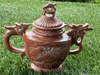 Full view of the front side of the teapot showing dragon shaped handle and spout, floral carvings on the body, and the lid with a dragon figure.