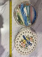 Photo showing both vintage decorative plates on a marble surface, including a measuring tape for scale.