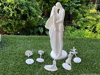Overview of the 7 Royal Doulton porcelain figurines including the large bride and groom, two birds, cat, ballet dancer, seated woman, and gymnast figurines, set outdoors on grass.