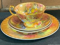 Stacked place setting with cup on top showing fruit pattern and gold handle.