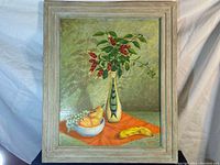 Framed still life painting showing a vase with red flowers, a bowl of fruit with pears, and a banana on an orange cloth.