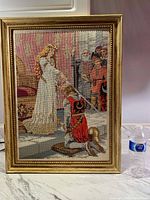 Full view of framed counted cross stitch depicting the knighting scene with a knight kneeling and a woman in white gown conducting the accolade.