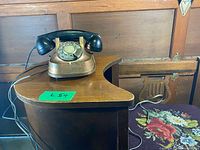 Vintage brass rotary dial telephone placed on a wooden surface and a floral fabric nearby.