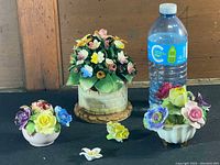 Overview of three vintage ceramic flower vases with artificial ceramic floral arrangements placed next to water bottle for scale