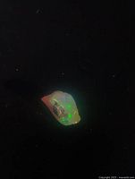 Photo of a small raw Ethiopian opal showing flashes of green color on a dark background.