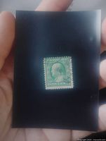 Bright green Benjamin Franklin one-cent postage stamp held on black backing showing perforations and cancellation marks.