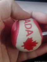 Close-up of the leather hacky sack ball held in hand showing the red and white panels with a maple leaf and the text "CANADA".