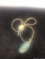 Gold plated twisted rope chain approximately 5 inches long with a green carved jade pendant. Chain has a round polished bead in the center with two small hanging chain tails.