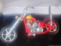 Front-left angle view of the red metal collectible chopper-style motorcycle toy showing the detailed V-twin engine, front forks, and spoked wheel.