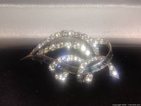 Close-up of silver-tone brooch showcasing clear rhinestones and central blue faux sapphire stone.