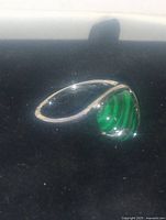 Close-up view of the silver ring with heart-shaped malachite cabochon stone showing vibrant green hues and banding, inside a jewelry box.