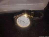 Front view showing white dial with black thin hour markers and gold-tone case.