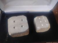 Pair of hand carved stone dice with irregular pips, shown inside a white box with black lining.