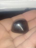 Polished black onyx gemstone palm stone held in hand, showing smooth, reflective surface with white sheen.