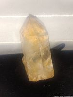 Single natural quartz crystal point displayed on a light surface showing its transparent to translucent clarity, natural facets, and pointed termination.