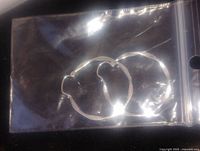 Pair of silver hammered hoop earrings visible in plastic zip bag under glare light reflection.