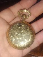 Front cover of pocket watch showing detailed floral and scroll engravings on gold plated case