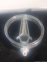 Front view of vintage Pontiac hood ornament badge showing circular frame and arrowhead emblem.