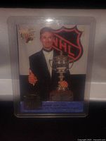 Photo of the front of the Wayne Gretzky hockey card showing him in a tuxedo holding the Lady Byng Memorial Trophy, giving a thumbs up, with NHL logo in the background.