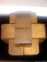 Top view of the wooden brain teaser puzzle showing interlocked blocks of light and dark wood forming a cross shape.