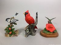 Group photo of all three ceramic bird figurines: cardinal, chickadee, and hummingbird with flower on wooden base.