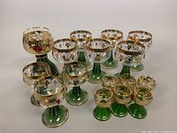 Full set of 16 Birkenau stemware glasses showing three size groups and green ribbed stems, grapevine motif, gold trim.