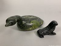 Both carved stone figurines displayed side by side, showing relative size and shape of duck and seal.