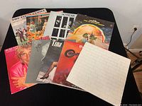 9 vinyl records spread out on black table including Pink Floyd, Meatloaf, Tina Turner, Rod Stewart, and others.