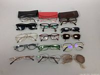Overview of 16 assorted eyeglasses frames in various colors and styles on a white surface with 3 eyeglass cases.