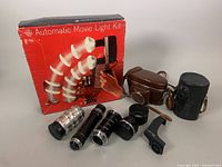 Overview of all items: three vintage camera lenses, two lens cases (brown and black), and the GE automatic movie light kit with box