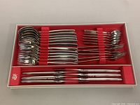 Full set of flatware pieces organized in a red-lined white box including spoons, forks, and knives.