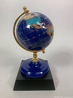 Photo of gem stone globe on black stand showing North and South America with gold-toned meridian.