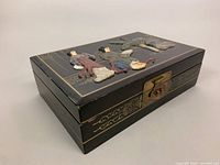 View of the jewelry box from an angled side showing the black lacquer surface and metal clasp, with visible wear on the edges.