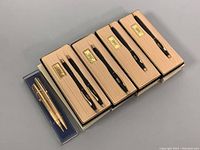 Photo of the entire lot showing six boxed pens and one boxed pen and pencil set, arranged linearly.